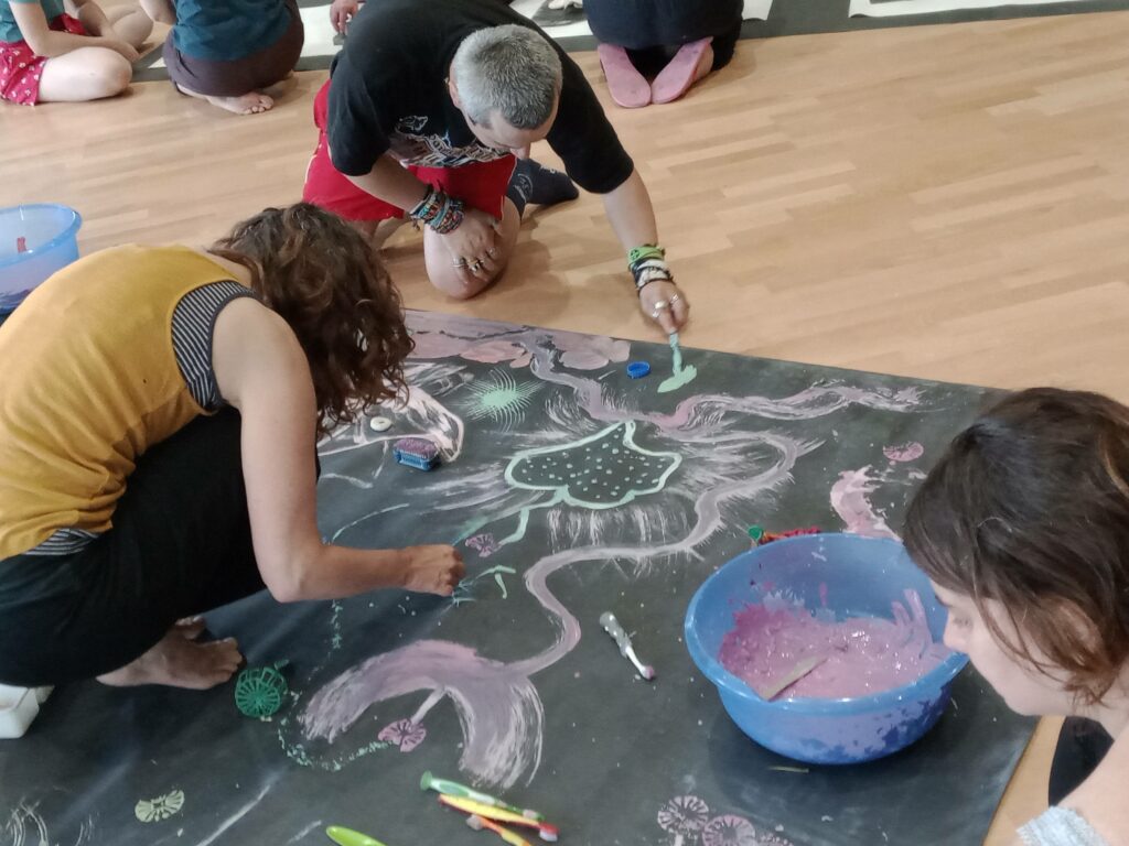 photo de 2 personnes accroupies par terre, elles dessinent à la craie sur un tableau noir au sol.